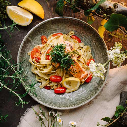 Ein Gericht zum hinknien – Lachs-Nudeln! Angerichtet mit frischer Zitrone, Cherrytomaten auf einem tiefen Teller.