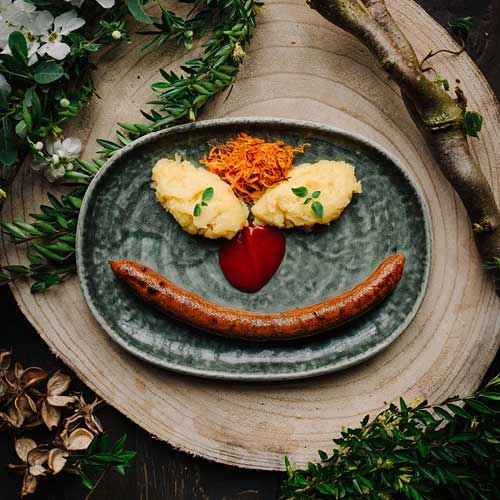 Das Kindergericht Thueringer Bratwurst mit Kartoffelbrei wird so angerichtet, dass es ein lächelndes Gesicht ergibt.