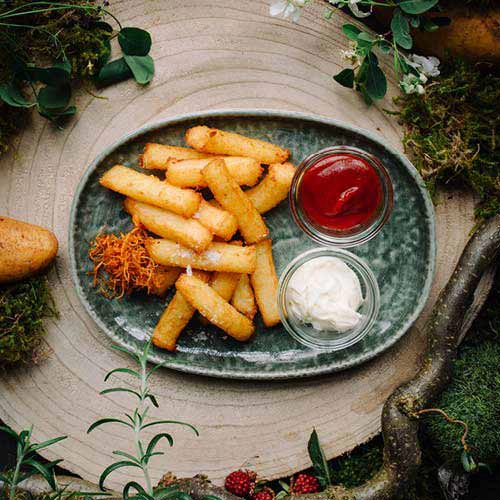 Das Kindergericht Klosspommes mit Dips auf einem Teller angerichtet. Drumherum Walddekorationen und Zutaten.