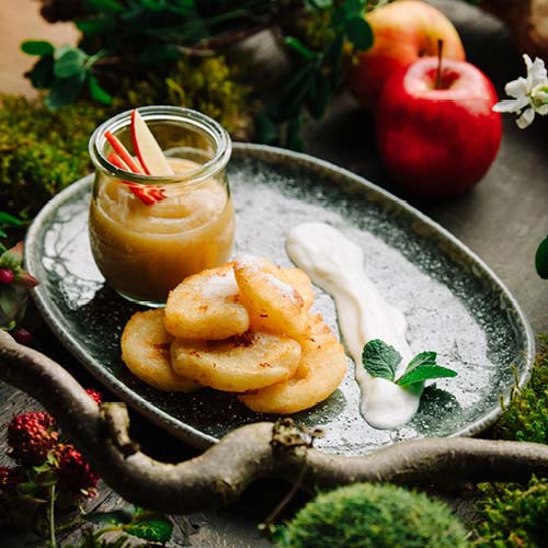 Ein gebratener Kloß mit saurer Sahne, Apfelmus und Zucker ist eine süße Köstlichkeit - kreativ angerichtet auf einem Teller.