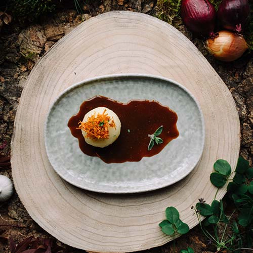 Das Kindergericht "Kleiner Baeren-Kloss mit Soss" ist auf einem Teller angerichtet. Drumherum sind Zutaten und Waldutensilien, wie Moos dekoriert.