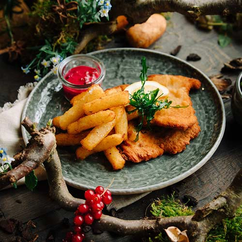 Ein typisch deutsches Gericht mit Schweineschnitzel, Kloßpommes und Preiselbeeren. Serviert auf einem Teller.