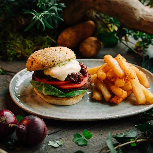 Ein Rinderpatty auf einem knusprigen Brötchen, verfeinert mit Cheddarschaum, Speckmarmelade, frischem Grünzeug und Kräuteraioli, ist ein echter Genuss! Dazu Kloßpommes, Dips – perfekt für alle Burger-Fans.