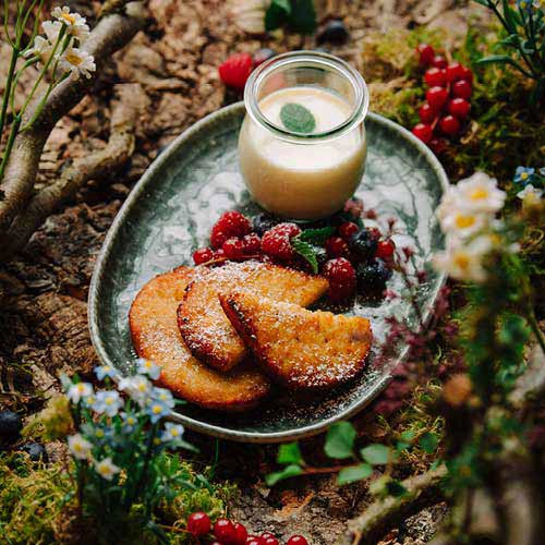 Das Dessert "Süsse Bäckchen" sind Quarktaler mit Waldbeeren und Vanillesauce. Angerichtet auf eibem grünen Teller.