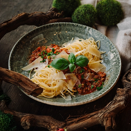 Ein typisches Gericht: Bolognese mit Spaghetti. Mit Parmesanflocken auf einem tiefen Teller angerichtet.