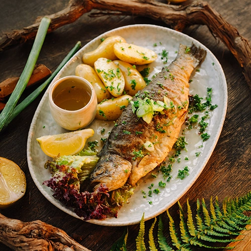Dieses Gericht zeigt eine Forelle, zart in Butter gebraten. Serviert auf einen schönen Teller mit Kartoffeln und Zitrone.