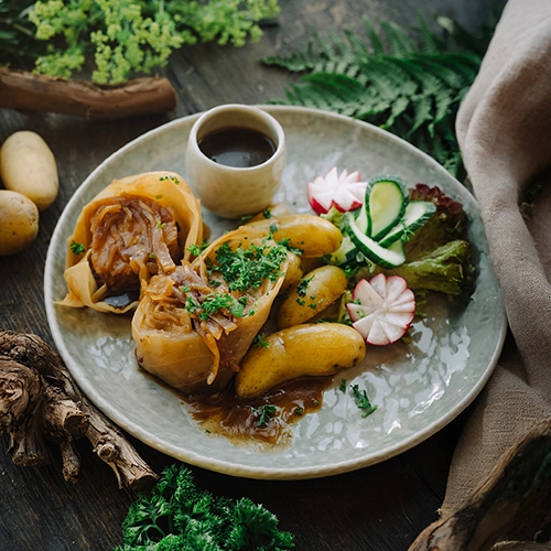 Ein leckeres Gericht mit Kohlrouladen, Kartoffeln und Krautsauce. Angerichtet auf einem Teller mit Walddekorationen drumherum.