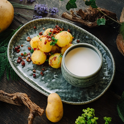 Das Gericht wird serviert mit Hüllerle mit Schinken, Zwiebeln und Buttermilch - angerichtet auf einem Waldboden mit rohen Zutaten drumherum.
