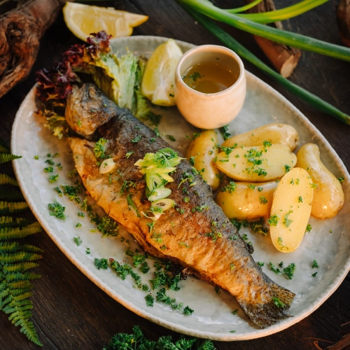 Dieses Gericht zeigt eine Forelle, zart in Butter gebraten. Serviert auf einen schönen Teller mit Kartoffeln und Zitrone.