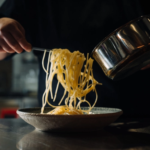 Eine Köchen richtet gerade Nudeln auf einem Teller an.