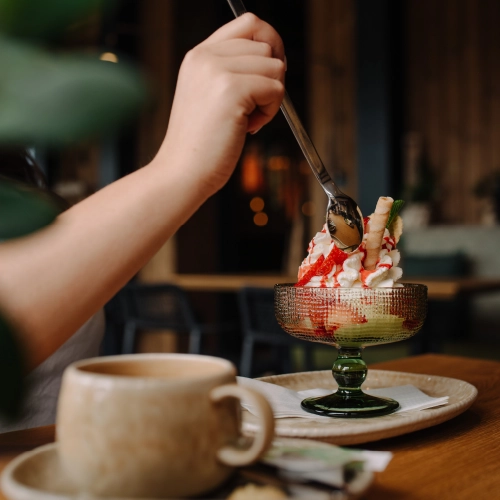 Ein Erdbeerbecher mit Sahne und Waffel wird gerade von einer Person gegessen.