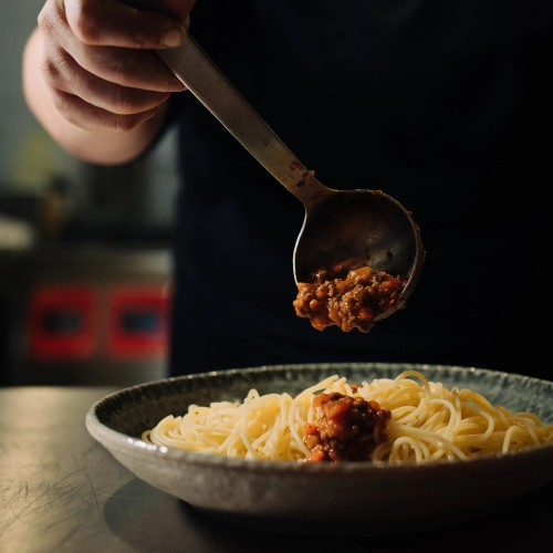 Die Köchin drapiert den Teller mit Bolognese.