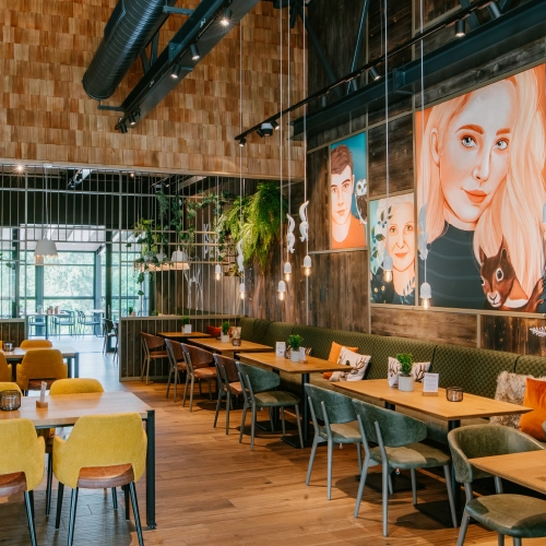 Das Restaurant verfügt über Sitzplätze und Tische. Es gibt gemütliche Plätze und kreative Wanddekorationen mit verschiedenen gezeichneten Personen.