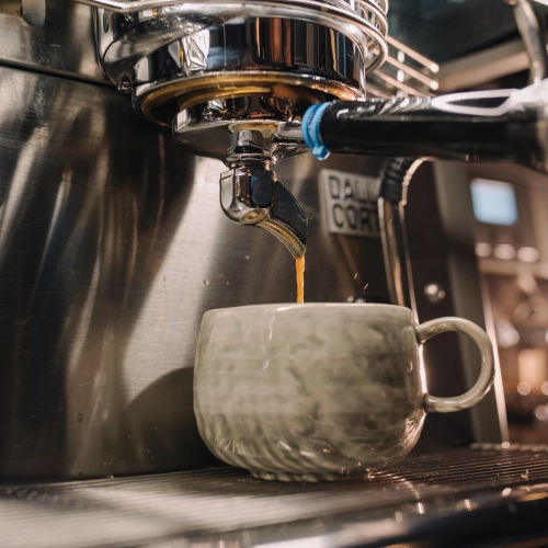 Kaffee läuft aus der Siebträgermaschine in eine graue Tasse.