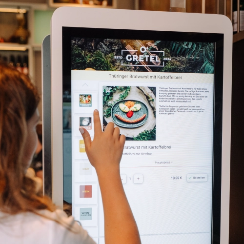 Das Terminal im Restaurant. Eine Frau bestellt gerade ein Gericht und toucht auf dem Bildschirm.